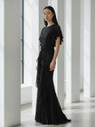 Model wearing a black floor-length dress pleated in a waterfall flowing design with bamboo jersey lining standing in a modern indoor setting