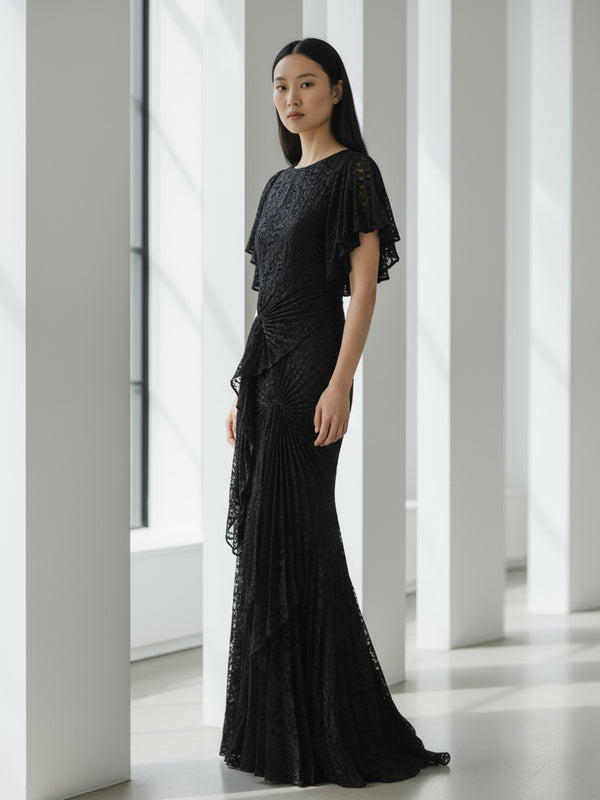 Model wearing a black floor-length dress pleated in a waterfall flowing design with bamboo jersey lining standing in a modern indoor setting