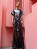 Model wearing a floor length metallic graphite chiffon dress, features delicate pleating in a flowing waterfall design, with a high neckline, slip on style, and adjustable waist tie.