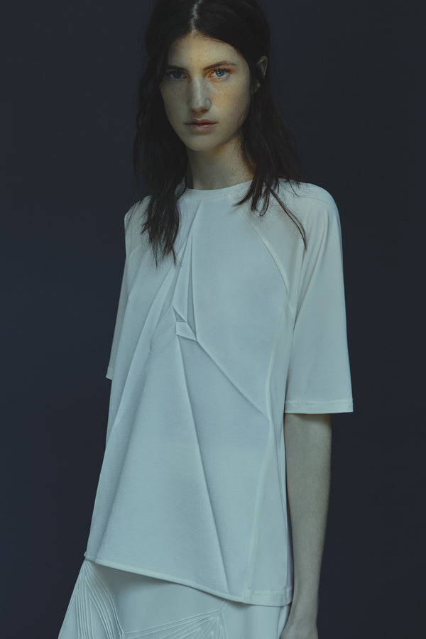 Model wearing an ivory shirt with a crack design against a dark background
