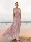 Model wearing a pink sleeveless velvet floor length dress pleated all over in a striking sunray design with side cut out at waist standing on a stone by the river 