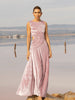 Model wearing a pink sleeveless velvet floor length dress pleated all over in a striking sunray design with side cut out at waist standing in a stone by the river