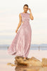 Model wearing a pink sleeveless velvet floor length dress pleated all over in a striking sunray design with side cut out at waist standing on a rock by the river