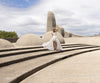 Model in Ivory-coloured dress with an elastic shirred contemporary pattern across the body standing on steps with large stone structures in the background