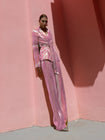 Model wearing a pink wrap-style sequin blazer with sunray stripes and matching wide-leg trousers lying against a pink wall