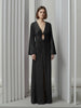 Model wearing a black velvet floor-length gown pleated all over in a striking sunray design with keyhole detail and long sleeves against a neutral background.