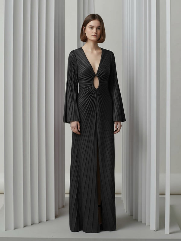 Model wearing a black velvet floor-length gown pleated all over in a striking sunray design with keyhole detail and long sleeves against a neutral background.
