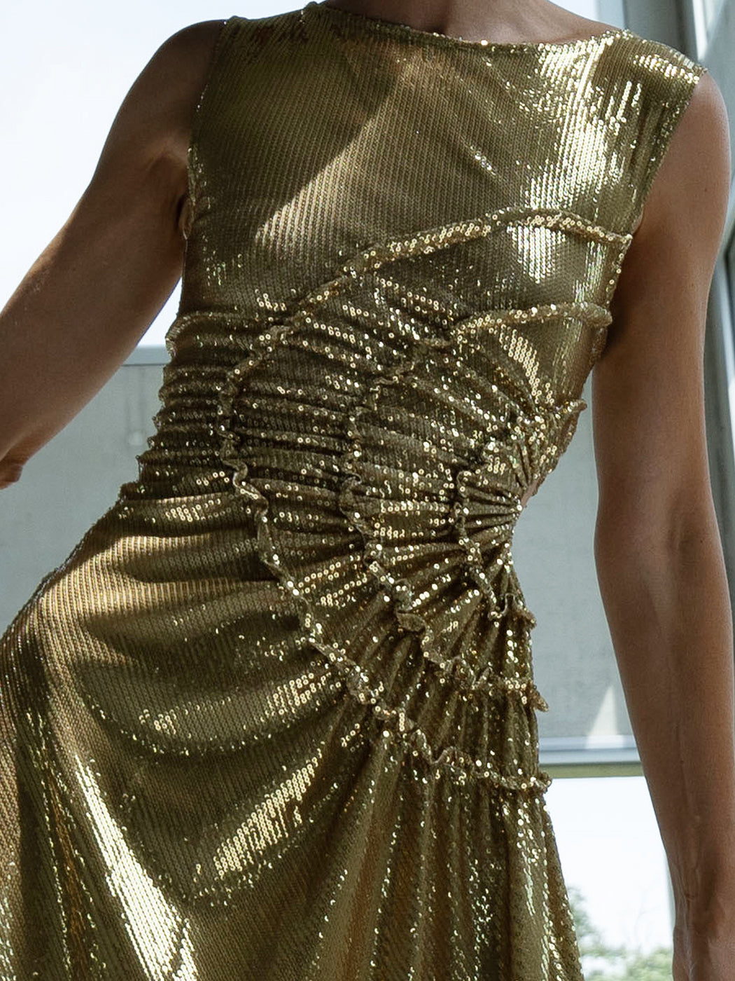 Close-up of a model wearing a gold sequin dress with gathered tuck detailing in a circular motion and adjustable waist cut out 