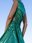 close-up of model wearing a green sequin dress with gathered tuck detailing in a circular motion and adjustable waist cut out against a clear blue sky