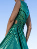 close-up of model wearing a green sequin dress with gathered tuck detailing in a circular motion and adjustable waist cut out against a clear blue sky