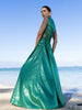 Model wearing a green dress statement dress adorned with all-over shimmering sequins, featuring circular gathered tuck detailing that creates a sculptural silhouette, a sleeveless design with a round neckline, an artfully ruched bodice, and an adjustable side waist cut-out. Standing on a beach with blue sky and ocean in the background.