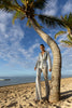 Model wearing a silver sequin blazer with a wrap style front and exaggerated shawl lapel, paired with high rise silver sequin trousers with a wide leg cut, creating a flattering, elongated, and statement making silhouette, standing on a beach with palm trees and ocean in the background.