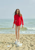 Model in a red jumper standing on a beach.