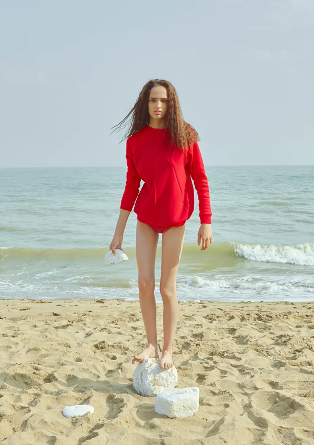 Model in a red jumper standing on a beach.