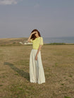 Model in a yellow top with geometric design and white skirt standing in a field.