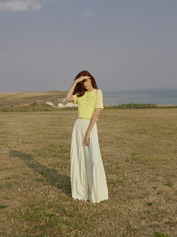 Model in a yellow top with geometric design and white skirt standing in a field.