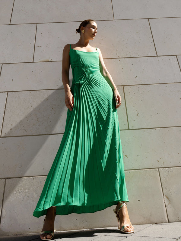 Model in a green georgette dress pleated in contrasting directions standing against a stone wall