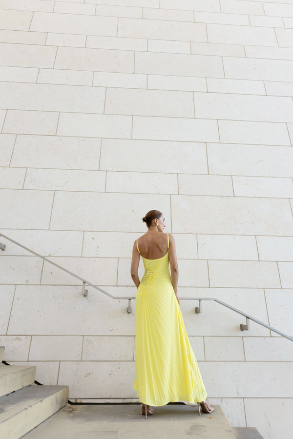 Model in a green georgette dress pleated in contrasting directions standing on a staircase against a light gray wall.