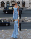 A grid photo where a model is wearing a blue floor-length pleated dress with a flowing waterfall design, standing on a city street with a black car in the background.