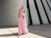 Model in a pink dress pleated in a sunray pattern on a French style baroque lace standing against a modern building.