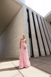 Model in pink sleeveless floor-length dress pleated in a sunray pattern with French baroque style lace standing outside a modern building.