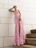 Model in pink sleeveless floor-length dress pleated in a sunray pattern with French baroque style lace standing on steps with a light-colored wall background