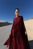 Model in a merlot coloured floor  length dress pleated in flowing waterfall design with wide sleeves and high neckline standing on a road with sand dunes and blue sky in the background