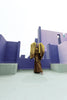 Model in a Gold liquid metallic floor-length dress pleated in a flowing waterfall design with long sleeves standing in a purple futuristic cityscape