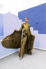 Model in a Gold liquid metallic floor-length dress pleated in a flowing waterfall design with long sleeves standing against a blue and white abstract wall.