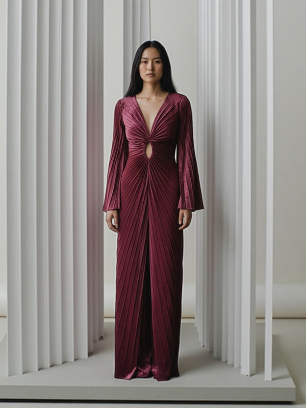 Model wearing a black velvet floor-length gown pleated all over in a striking sunray design with keyhole detail with long sleeves in a minimalistic setting.