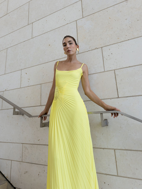 Model in a green georgette dress pleated in contrasting directions standing against a light stone wall.